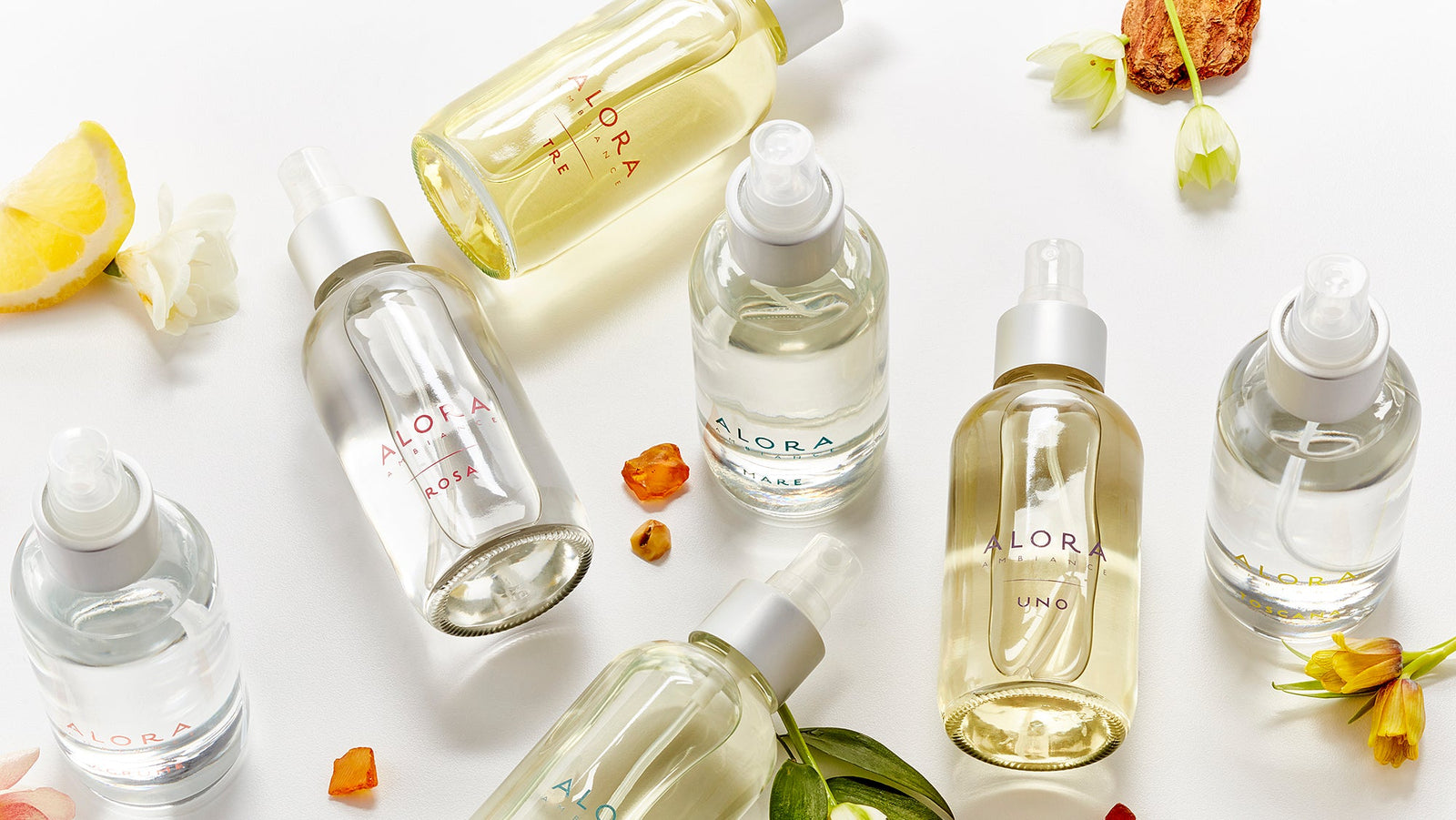 Room spray bottles in various scents laying about on a white background with floral, citrus, and warm notes laying around.