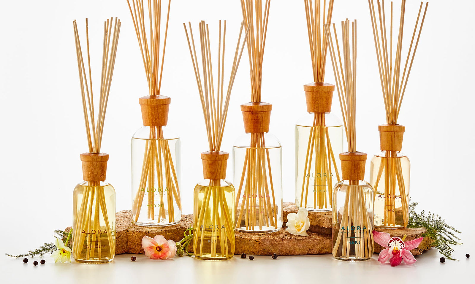 Collection of 7 reed diffusers with various flowers arranged around them.