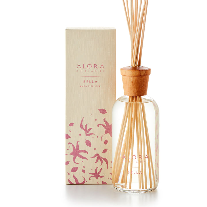 Alora Ambiance 16oz Bella reed diffuser with glass bottle and wooden cap next to tan box with pink floral pattern on it.
