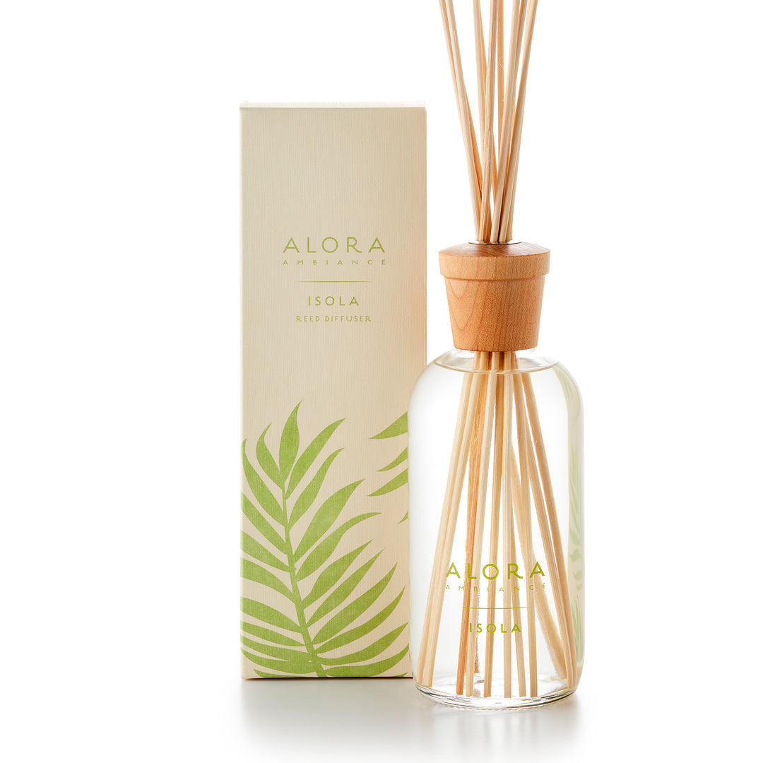 Alora Ambiance 16oz Isola reed diffuser with glass bottle and wooden cap next to tan box with green tropical leaf pattern on it.