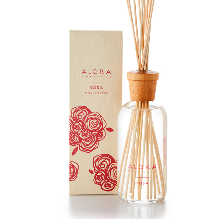 Alora Ambiance 16oz Rosa reed diffuser with glass bottle and wooden cap next to tan box with pink rose pattern on it.