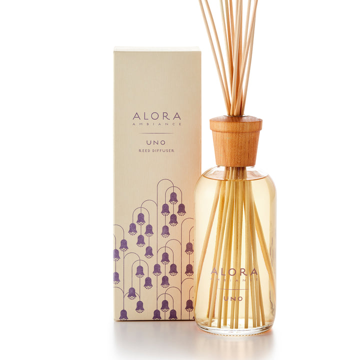 Alora Ambiance 16oz Uno reed diffuser with glass bottle and wooden cap next to tan box with purple Lily of the Valley flower pattern on it.