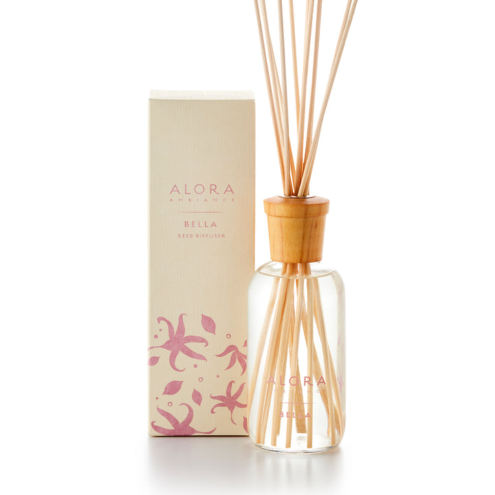 Alora Ambiance 8oz Bella reed diffuser with glass bottle and wooden cap next to tan box with pink floral pattern on it.