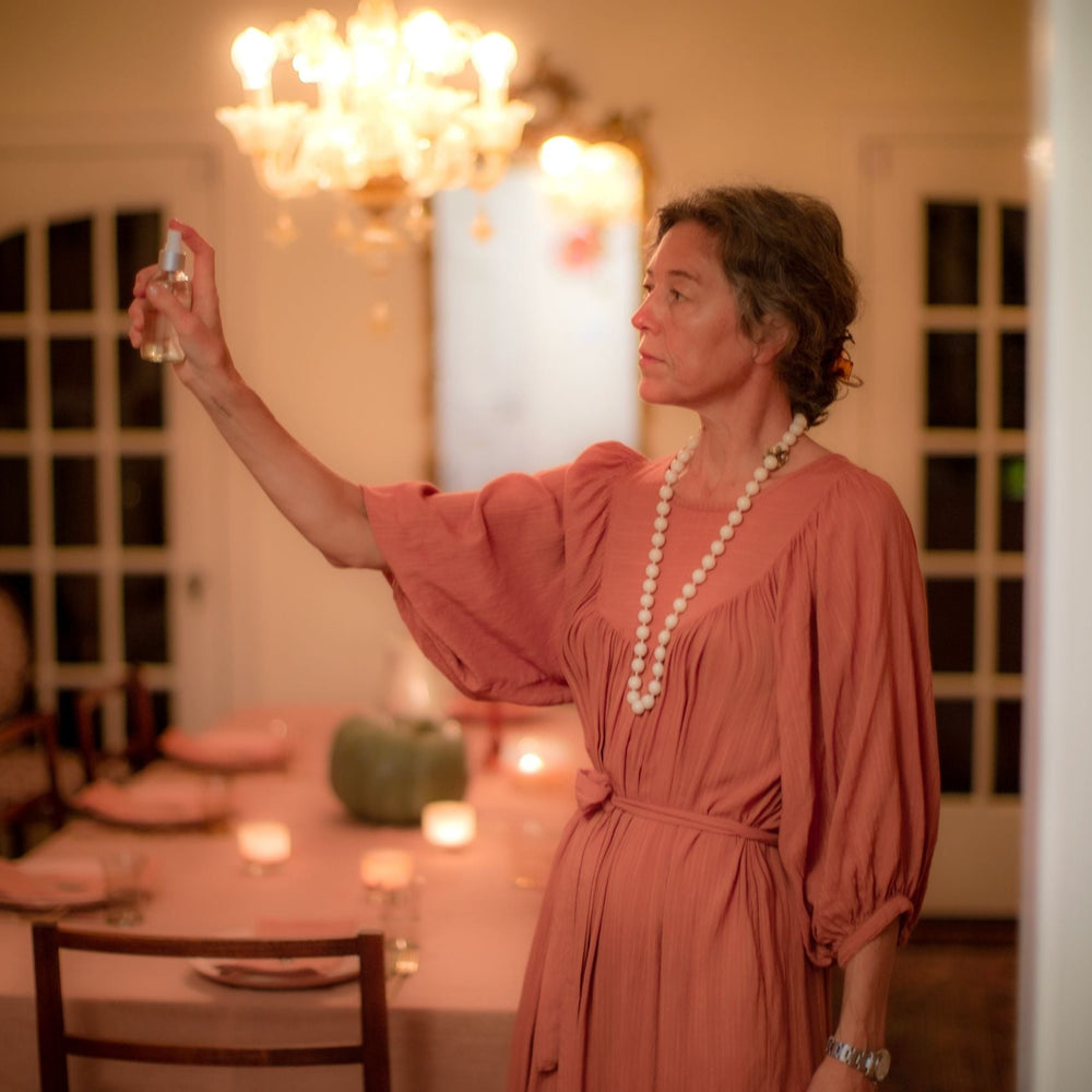 Woman in pink dress spraying room spray in dining room