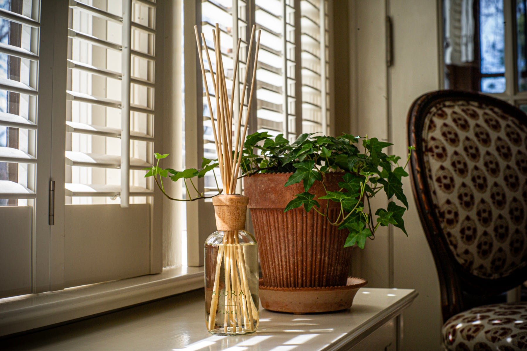 Reed diffuser on window sill next to terracotta pot filled with ivy.