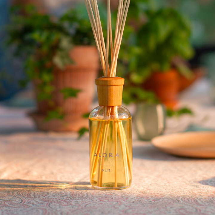 Due reed diffuser on pink tablecloth with a ivy plant in a terracotta pot in the background