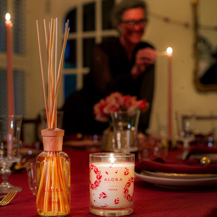 Woman lighting taper candle on a set table, Festa diffuser and candle sit in the foreground
