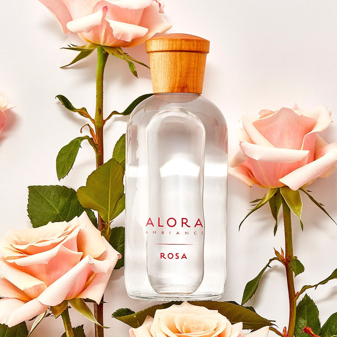 Rosa glass reed diffuser bottle surrounded by pink roses