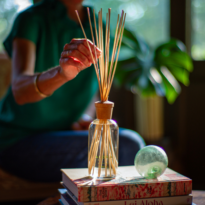 Woman touching reeds on a Isola reed diffuser that is sitting on a stack of books