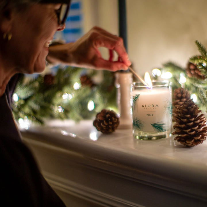 Woman lighting a Pino candle sitting on a mantle