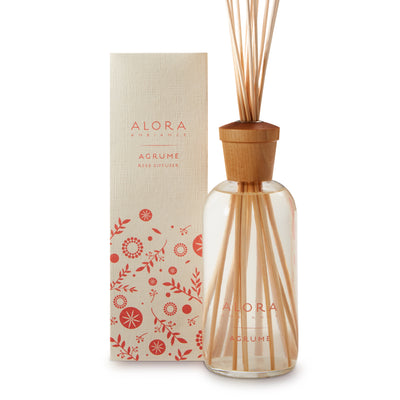 Glass bottle filled with clear, liquid fragrance, topped with wood cap with reeds passing through cap into liquid. Bottle says “Alora Ambiance” and “Agrume” and is next to tan box