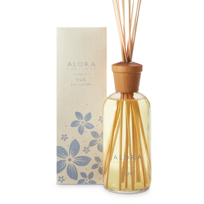 Glass bottle filled with liquid fragrance, topped with wood cap with reeds passing through cap into liquid. Bottle next to tan box says “Alora Ambiance” and “Due”