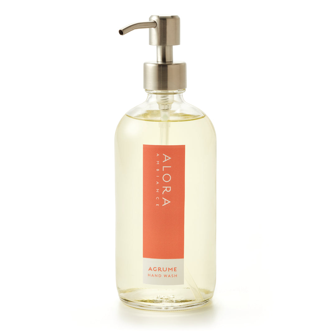 Tall glass bottle topped with a silver pump and filled with clear, liquid hand wash with label that says “Alora Ambiance” and “Agrume Hand Wash” on the front