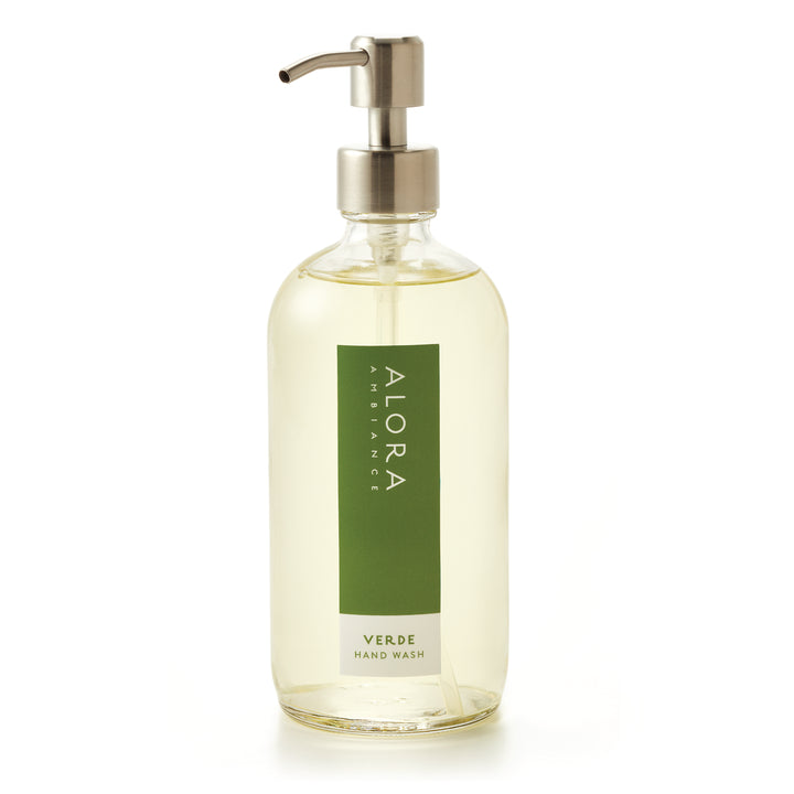 Tall glass bottle topped with a metal pump and filled with clear, liquid hand wash with label that says “Alora Ambiance” and “Verde Hand Wash” on the front