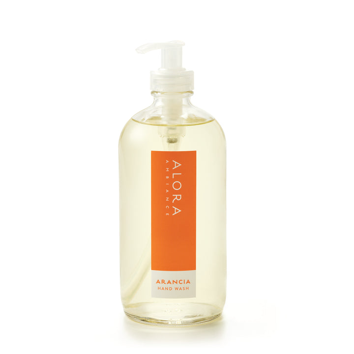 Tall glass bottle topped with a plastic pump and filled with clear, liquid hand wash with label that says “Alora Ambiance” and “Arancia Hand Wash” on the front