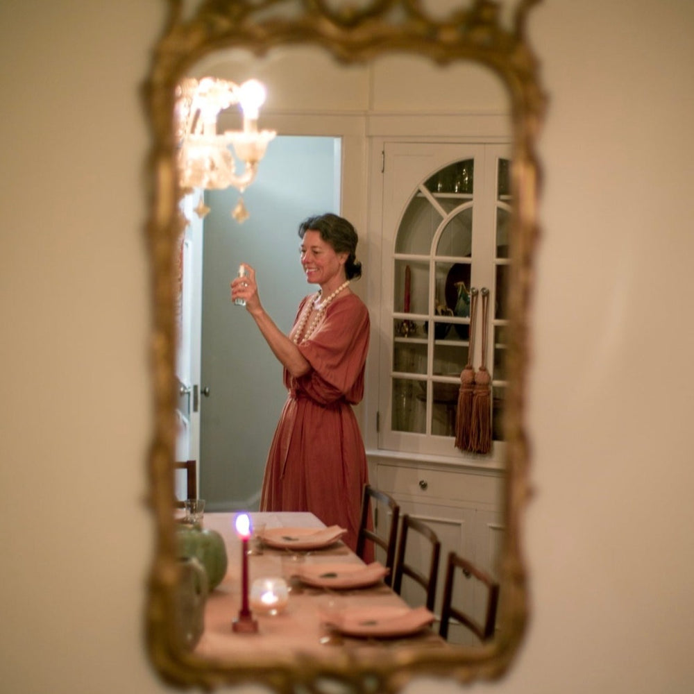 Woman in front of a set dinner table spritzing a room spray