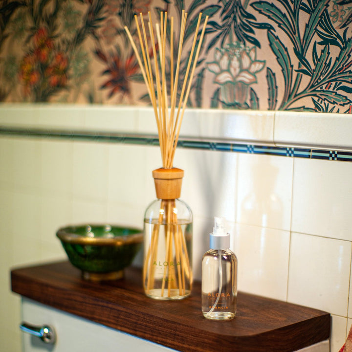 Arancia room spray and Isola reed diffuser sitting on a back of a toilet seat