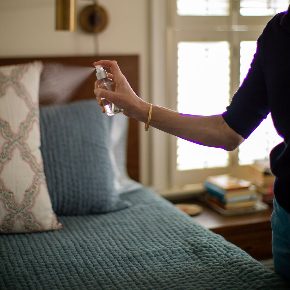 Woman spritzing room spray onto blue bedding