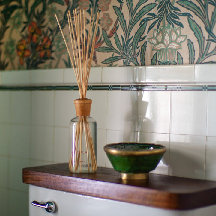 Agrume reed diffuser sitting on a shelf on the back of a toilet in a bathroom