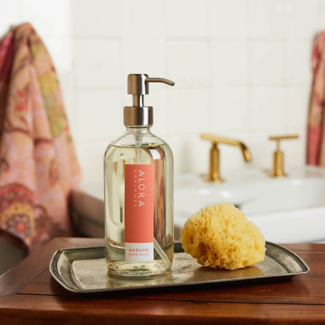 Agrume hand wash bottle on silver tray with sponge in a bathroom.