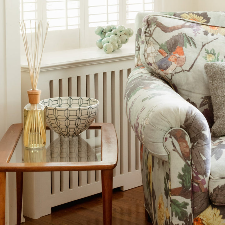 Due reed diffuser on a end stand next to a floral patterned arm chair