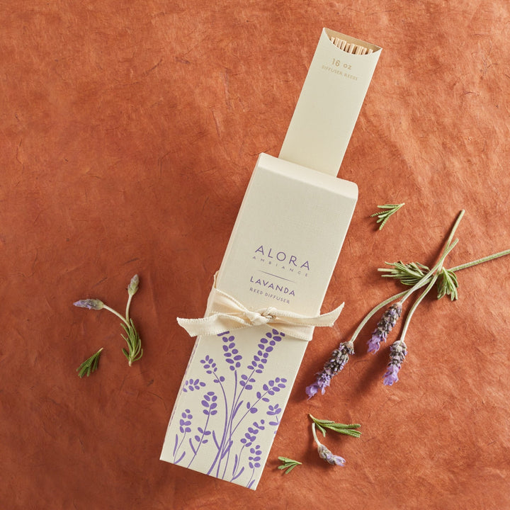 Lavanda reed diffuser box and reeds in package all tied up with a cream ribbon. Sprigs of lavender surround box.