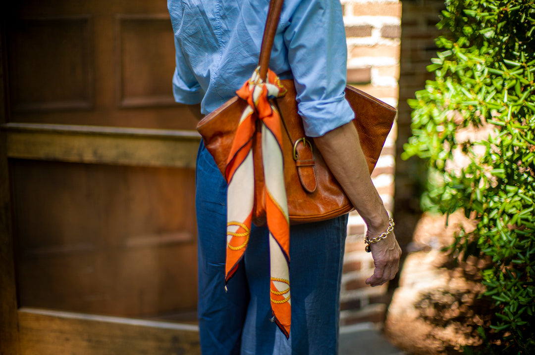 Woman holding a leather bag with an orange scarf tied to it