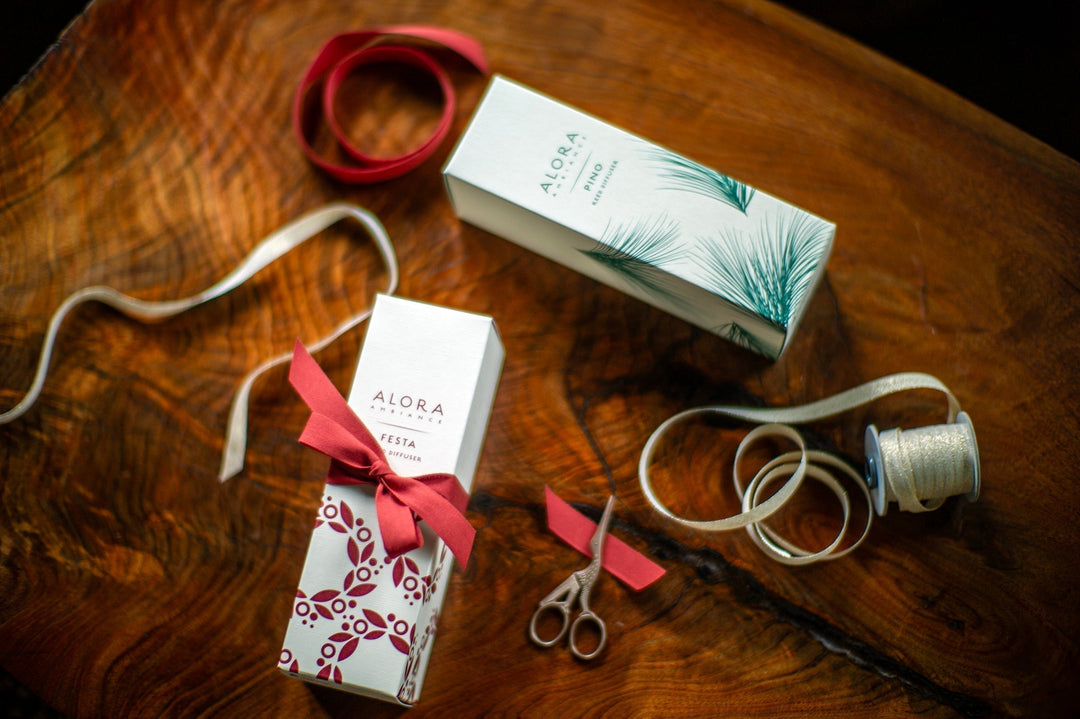 Festa diffuser box wrapped with red ribbon lying next to a Pino diffuser box on a wooden table
