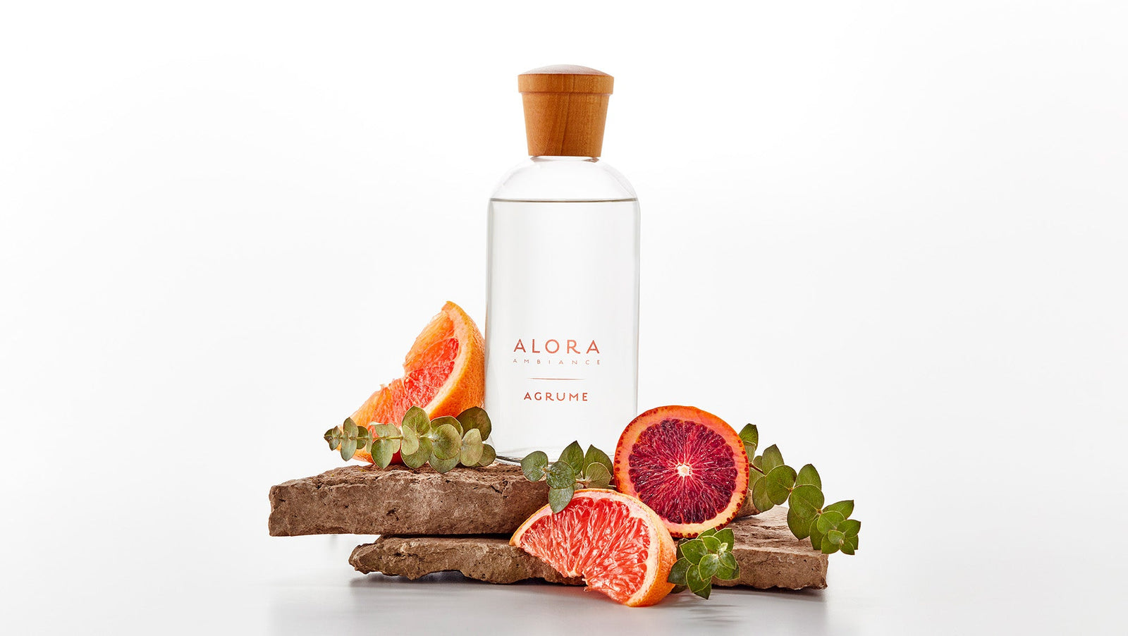 Agrume diffuser bottle sitting on a stone next to eucalyptus sprigs and grapefruit and orange slices