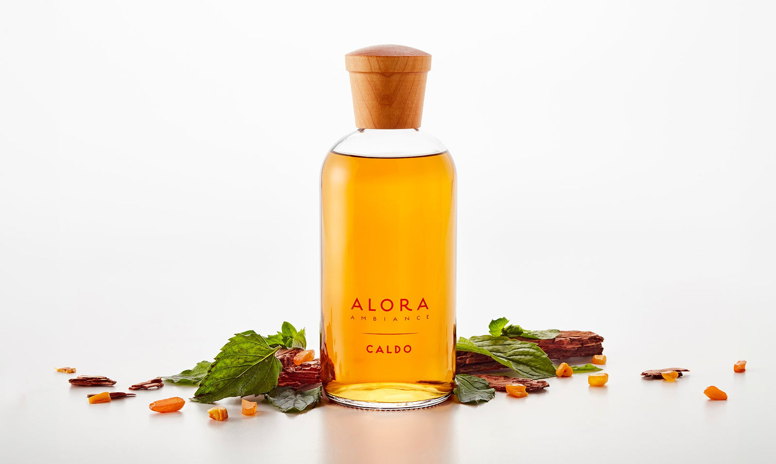 Caldo diffuser bottle next to patchouli leaves and sandalwood and amber pieces