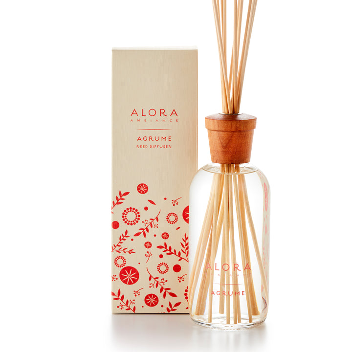 Alora Ambiance 16oz Agrume reed diffuser with glass bottle and wooden cap. Bottle is standing next to tan box with pink floral pattern on it.