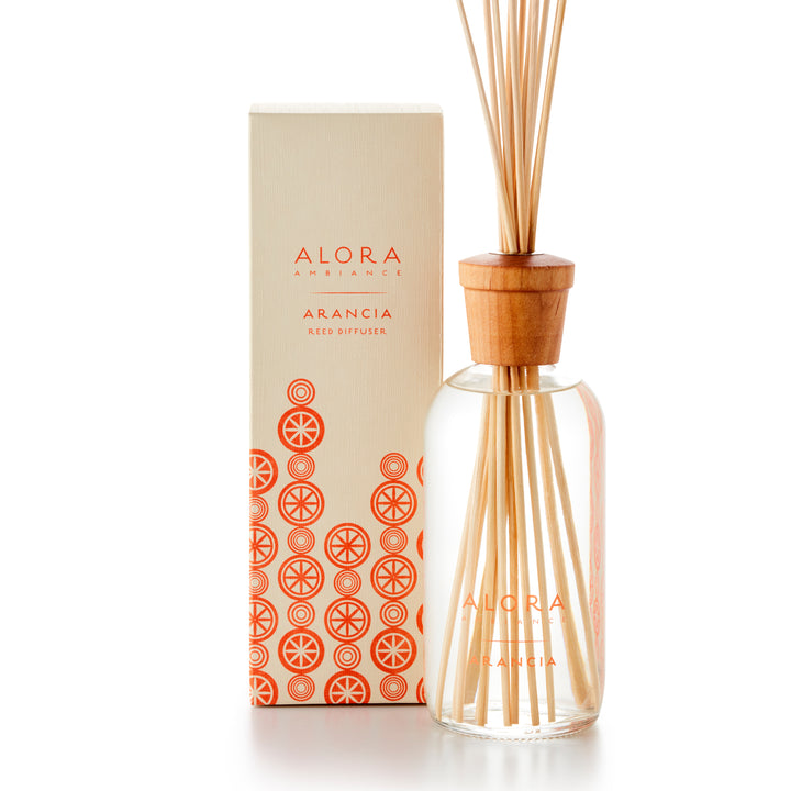Alora Ambiance 16oz Arancia reed diffuser with glass bottle and wooden cap  next to tan box with pattern of oranges on it.