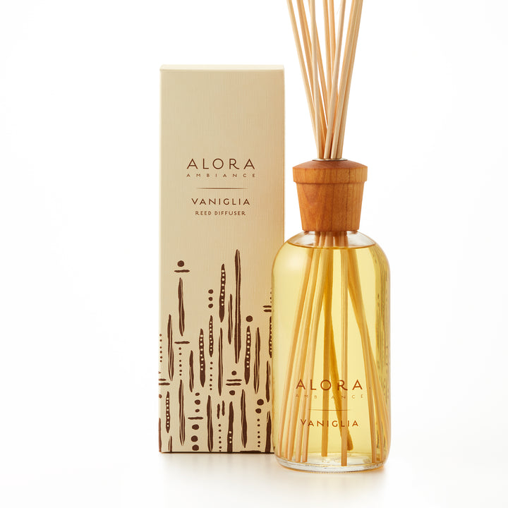 Alora Ambiance 16oz Vaniglia reed diffuser with glass bottle and wooden cap next to tan box with a brown striped and dotted pattern on it.