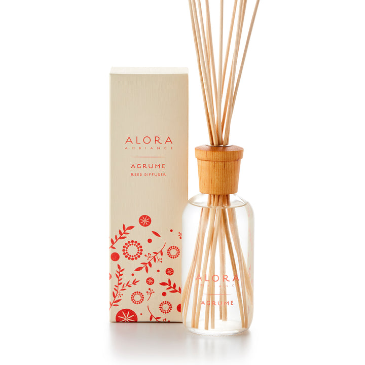 Alora Ambiance 8oz Agrume reed diffuser with glass bottle and wooden cap. Bottle is standing next to tan box with pink floral pattern on it.