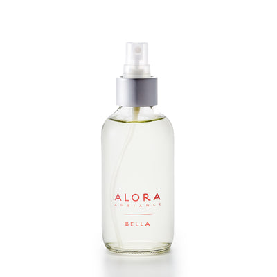 Small, glass spray bottle with "Alora Ambiance" and "Bella" written in pink font on the front