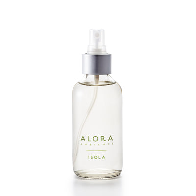 Small, glass spray bottle with "Alora Ambiance" and "Isola" written in green font on the front, bottle is filled with clear liquid fragrance