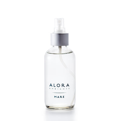 Small, glass spray bottle with "Alora Ambiance" and "Mare" written on the front in dark blue font, bottle is filled with clear liquid fragrance