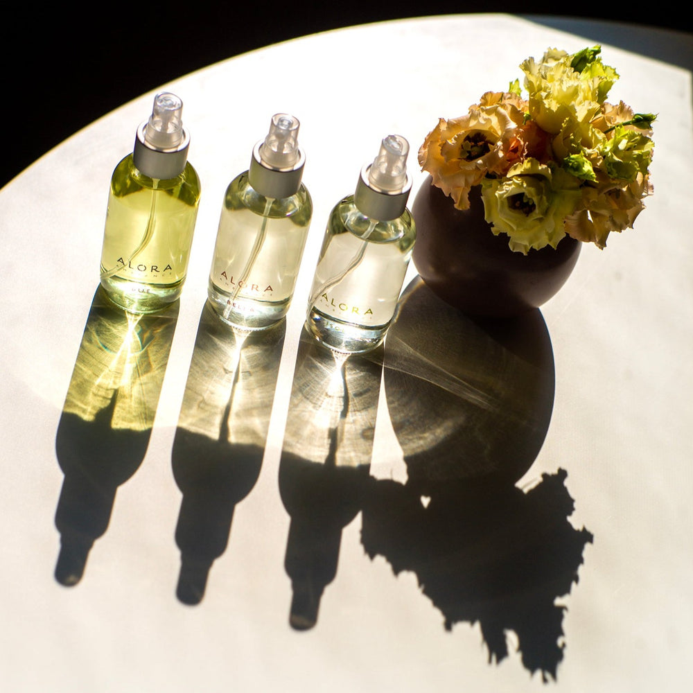 Due, Bella, and Isola room spray on white table with sunshine shining through the glass bottles