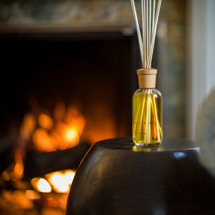 Festa reed diffuser in front of a lit fireplace