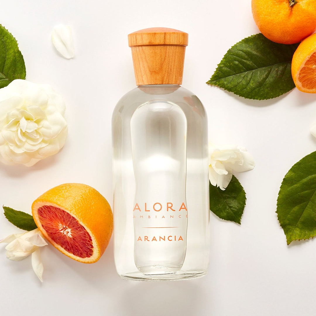 Arancia diffuser bottle laying next to oranges and gardenia flowers