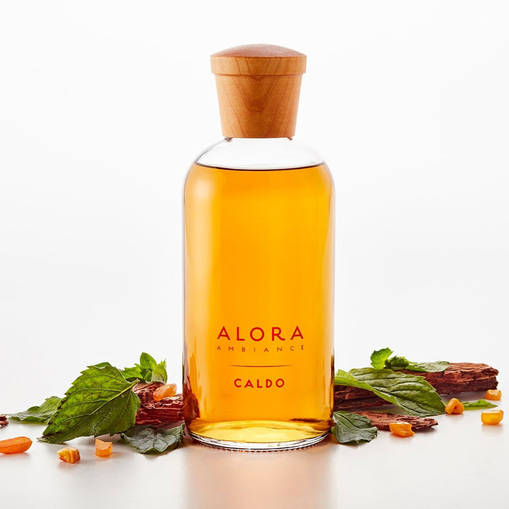 Caldo diffuser bottle next to patchouli leaves, sandalwood pieces, and pieces of amber