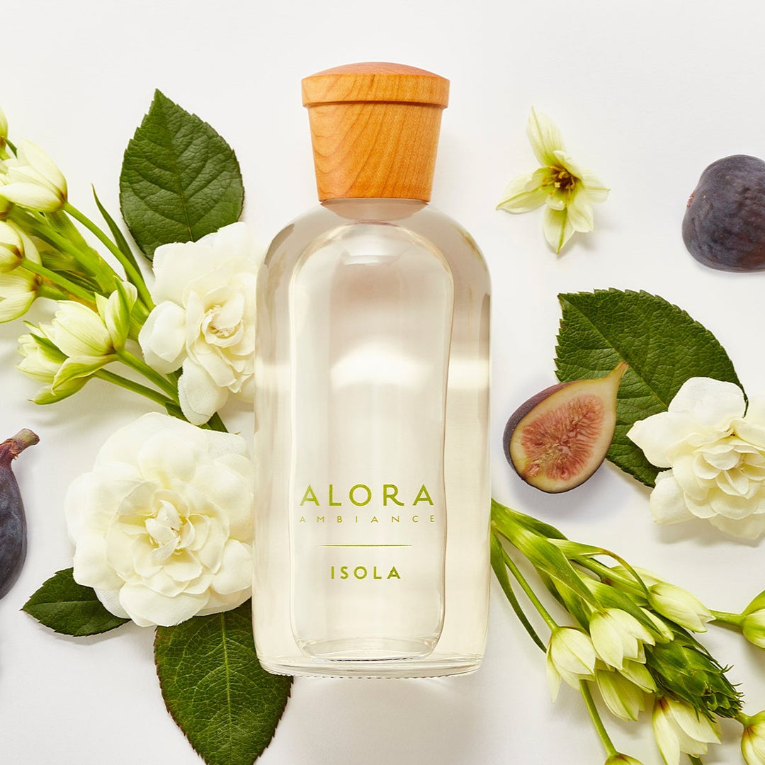 Isola diffuser bottle laying next to figs and tuberose and gardenia flowers