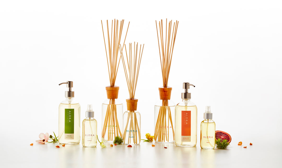 An array of reed diffusers, hand wash bottles, and room spray bottles lined up in front of a white background