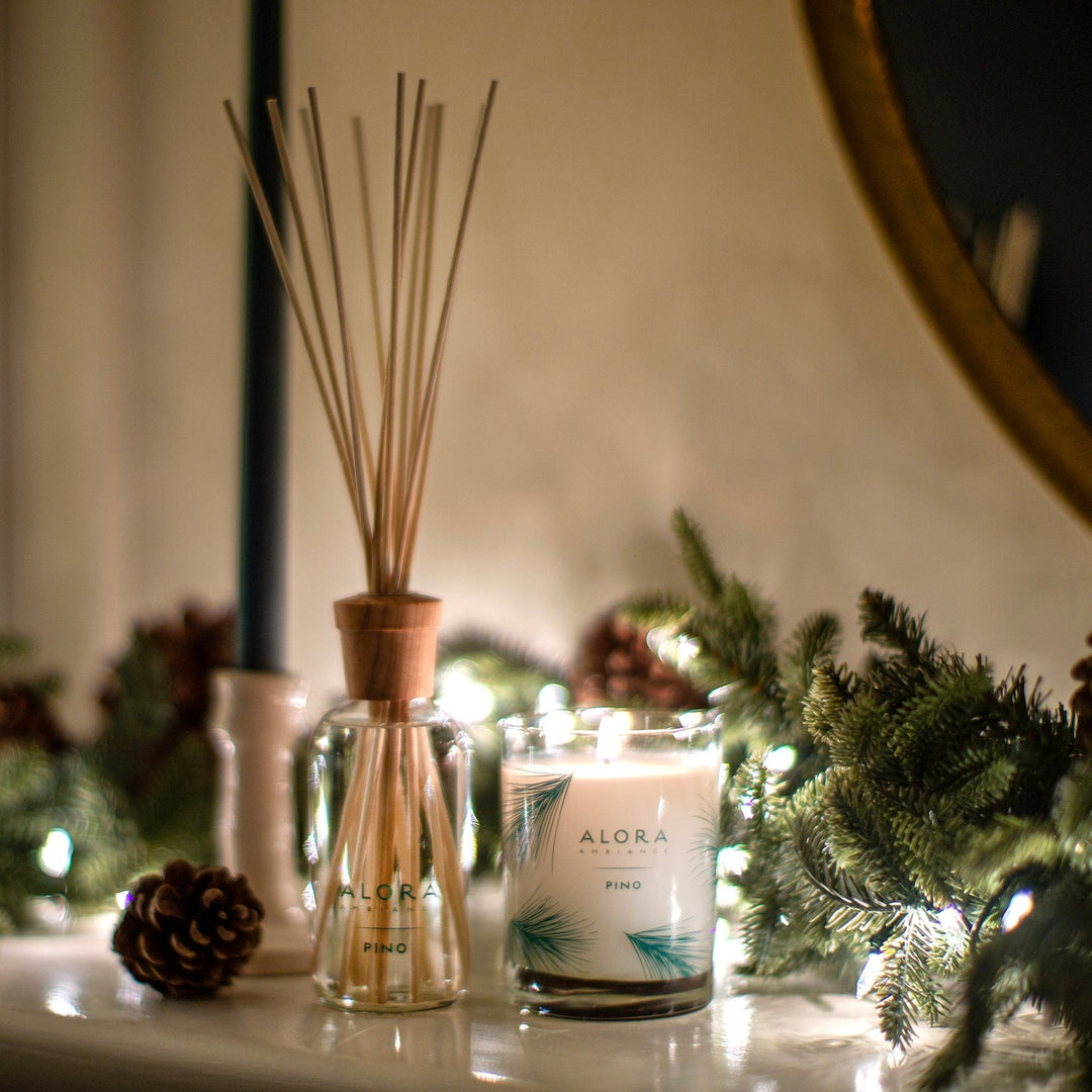 Pino diffuser and candle on a mantle decorated with holiday greenery and pine cones