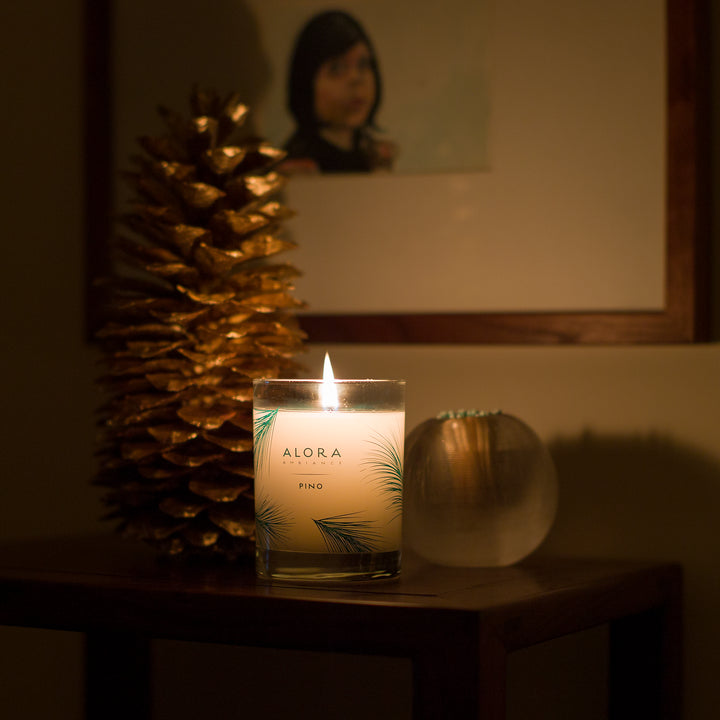Lit Pino candle glowing in a dark room next to a gold pine cone