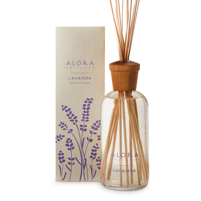 Glass bottle filled with liquid fragrance, topped with wood cap with reeds passing through cap into liquid. Bottle by tan box says “Alora Ambiance” and “Lavanda”