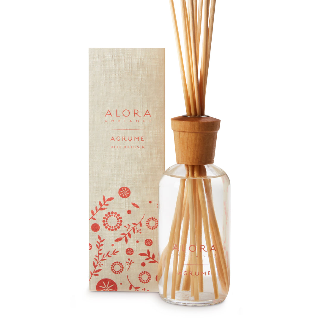 Glass bottle filled with clear, liquid fragrance, topped with wood cap with reeds passing through cap into liquid. Bottle says “Alora Ambiance” and “Agrume” and is next to tan box