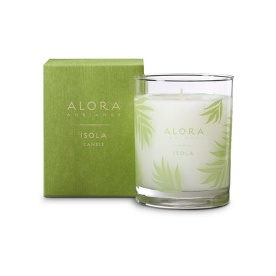 White-colored candle in glass jar that says “Alora Ambiance” and “Isola” and sits next to green box that says “Alora Ambiance” and “Isola Candle”