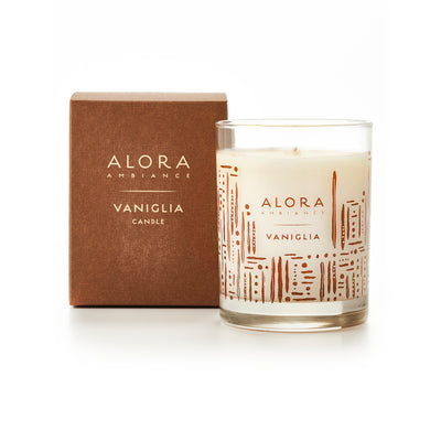 White-colored candle in glass jar that says “Alora Ambiance” and “Vaniglia” and sits next to brown box that says “Alora Ambiance” and “Vaniglia Candle”