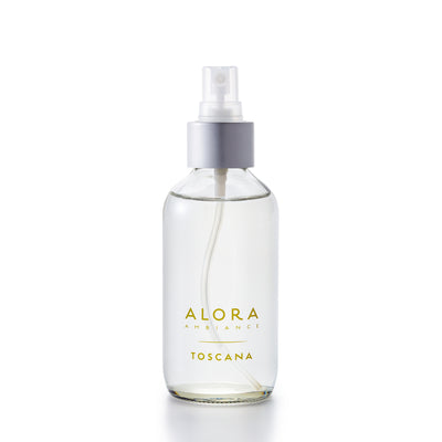 Small, glass spray bottle with "Alora Ambiance" and "Toscana" written on the front, bottle is filled with clear liquid fragrance